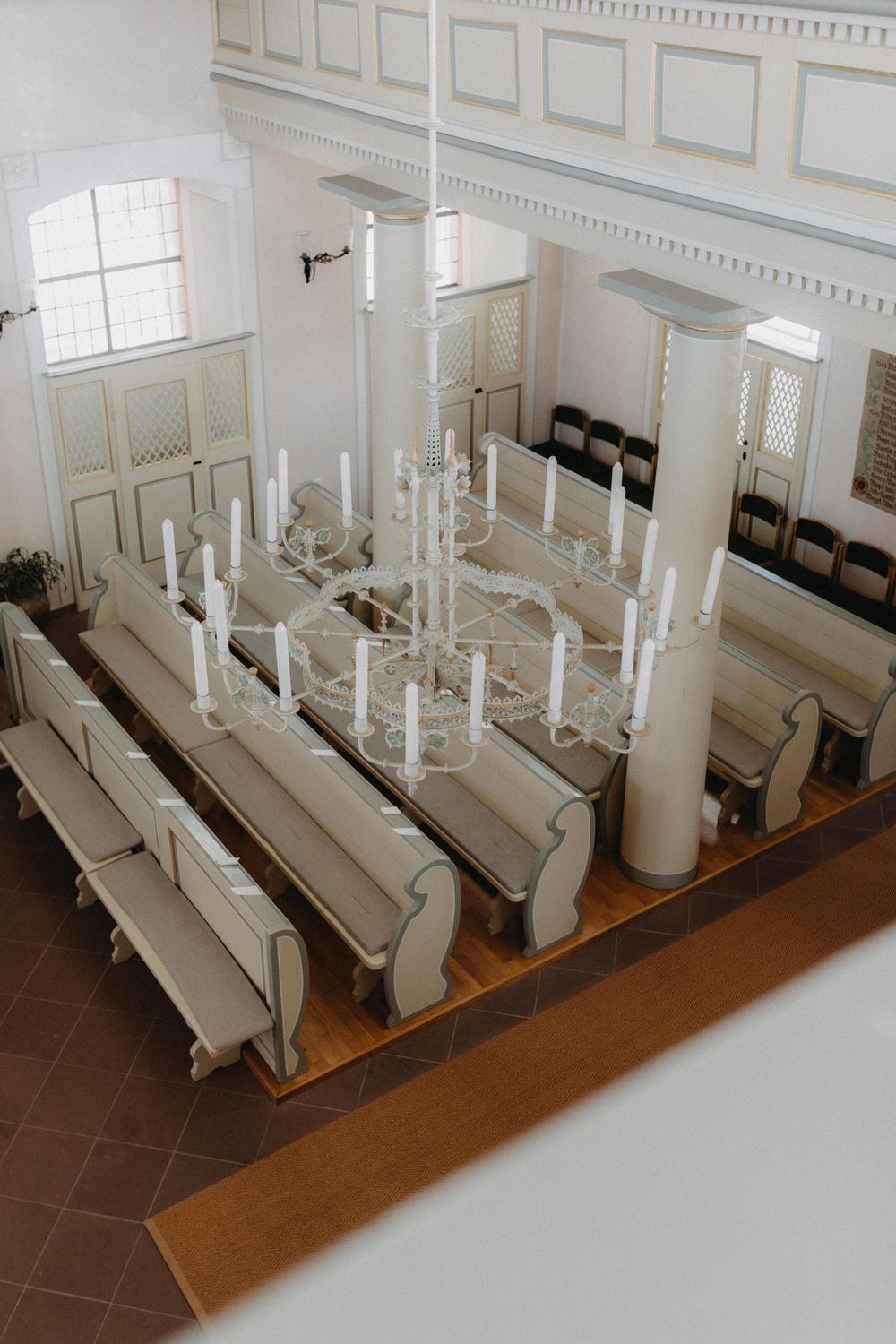 White church interior with wooden pews and elegant chandelier viewed from above.