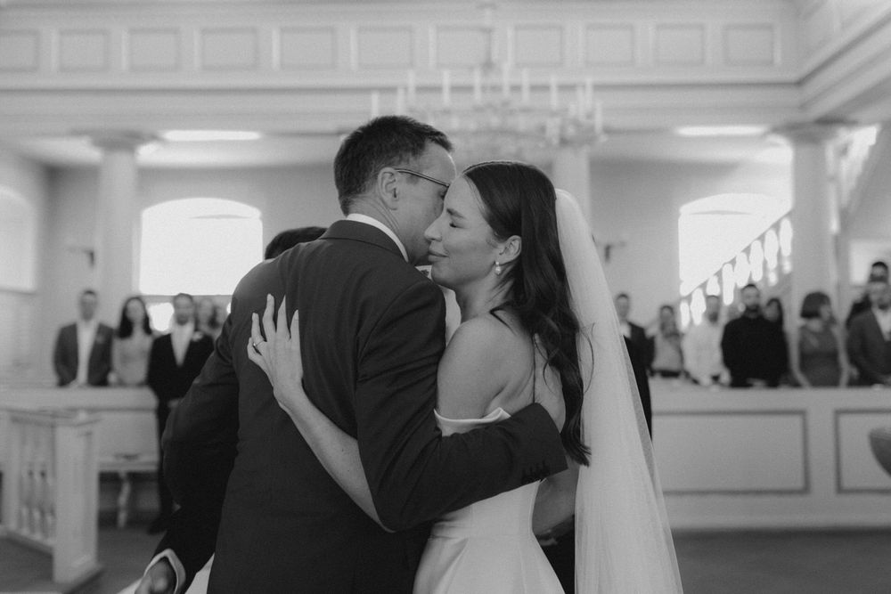 A romantic black and white wedding moment as newlyweds share a kiss during their ceremony in an elegant venue.