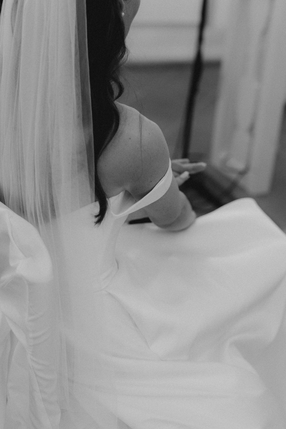 Black and white detail shot of a bride's back in a white wedding gown with flowing veil.
