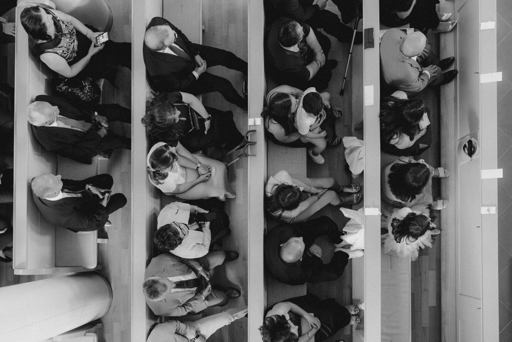 Overhead black and white view of wedding guests seated in church pews during a ceremony.