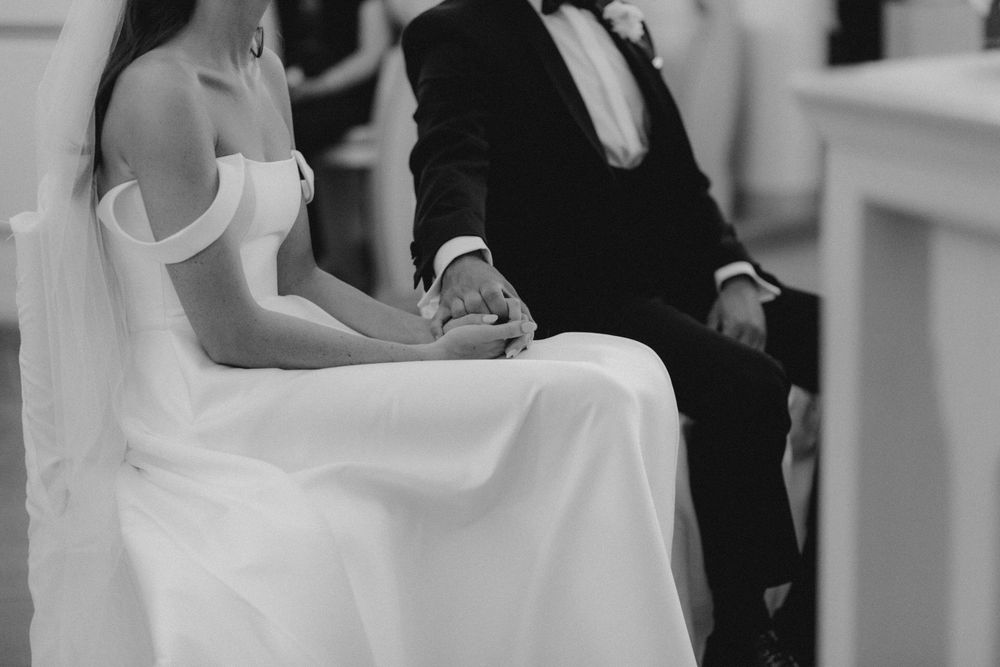 Close-up black and white shot of newlyweds holding hands during their wedding ceremony.