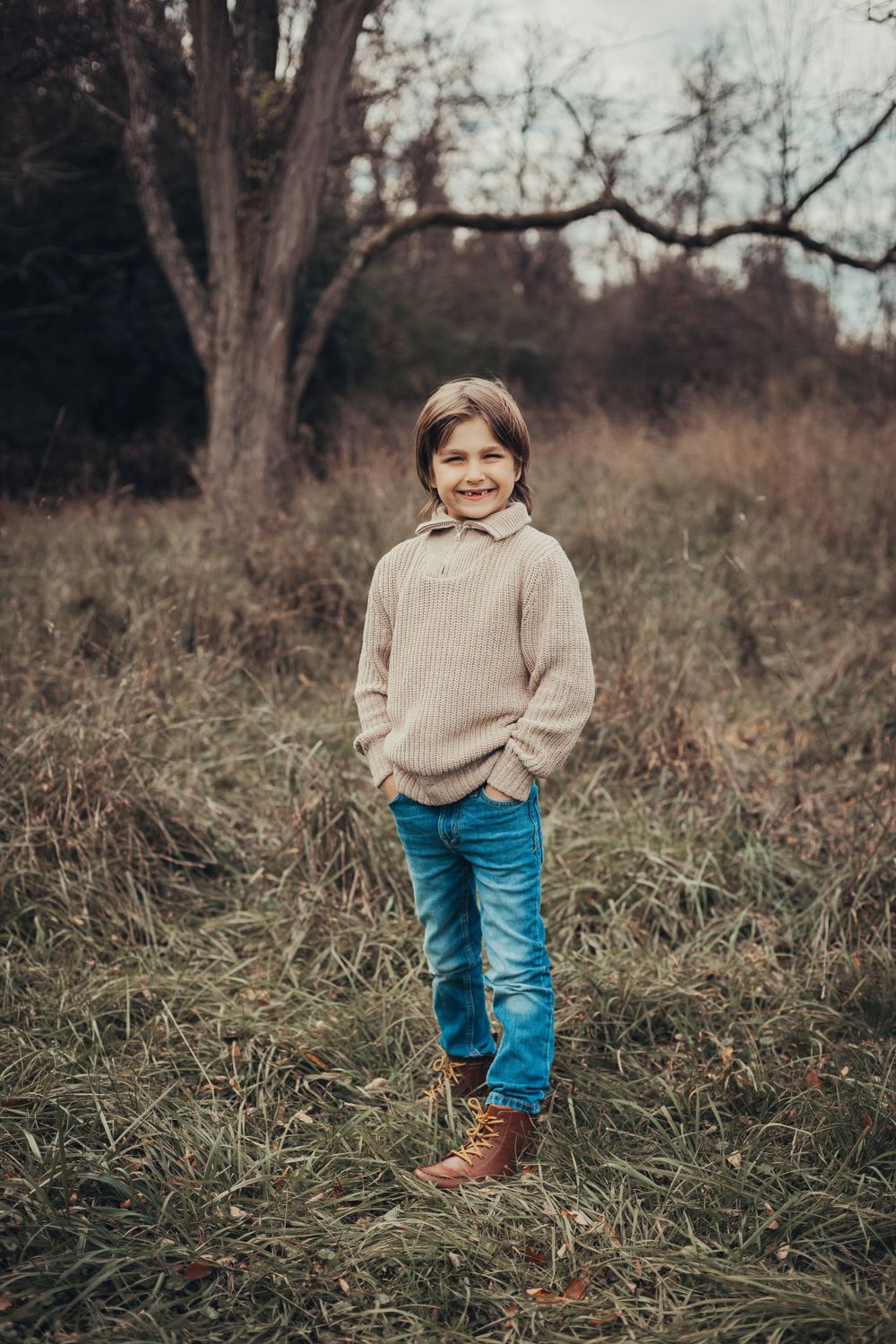 A casual outdoor portrait featuring a cozy beige sweater and blue jeans against an autumn backdrop.