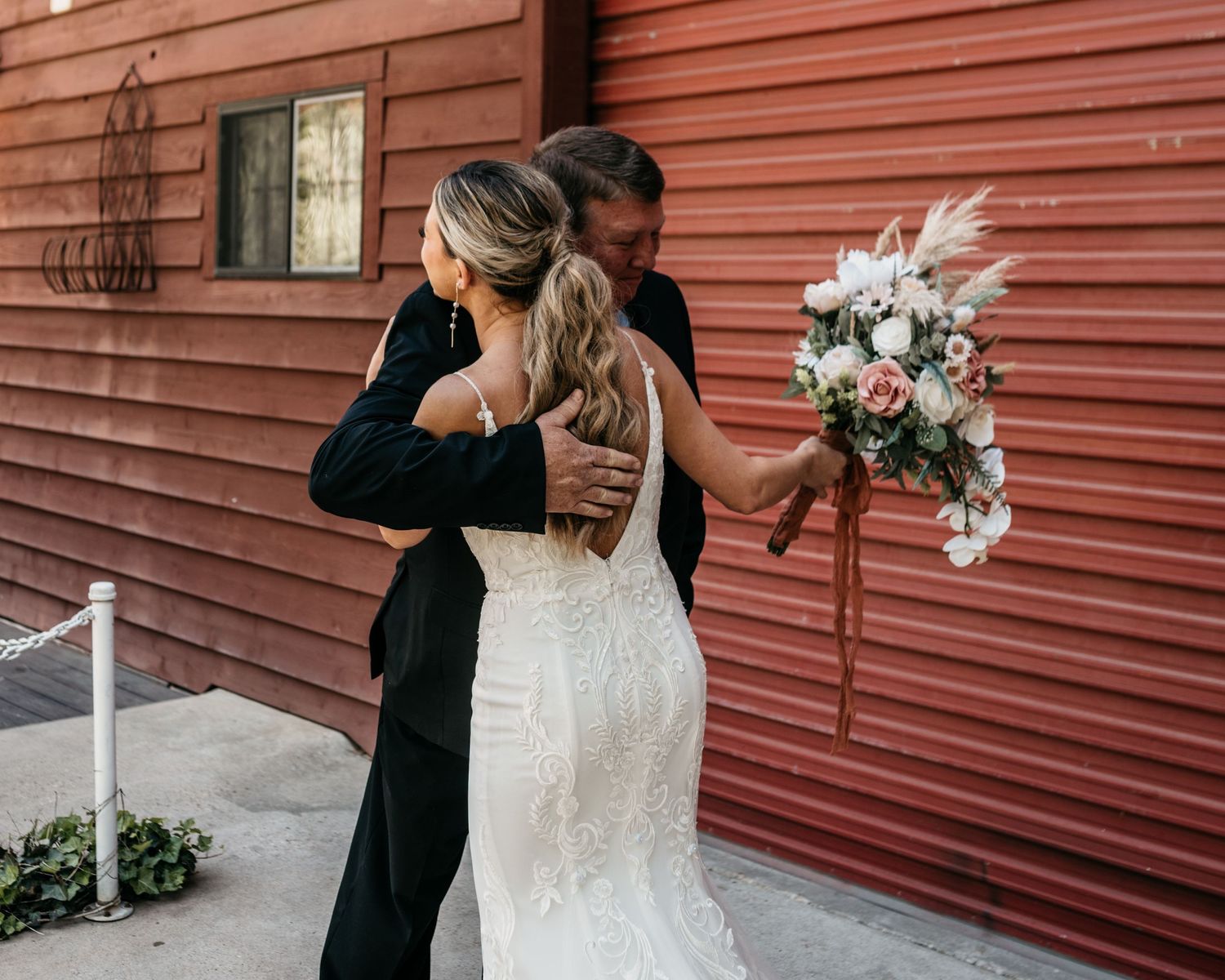 Intimate first look embrace between bride and groom against rustic red wall.