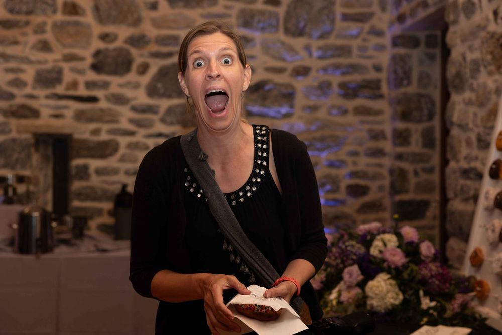 Photographer with animated expression works at reception with stone wall backdrop.