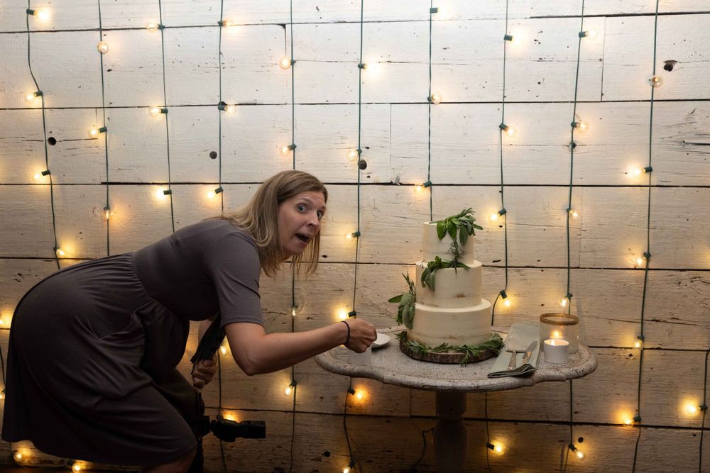 Photographer adjusting cake display against wall with string lights in dark setting.