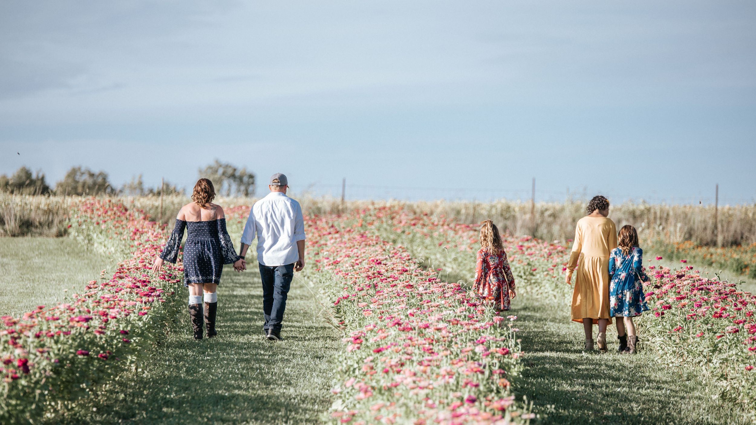 People walking through a vibrant field of red wildflowers on a sunny day.