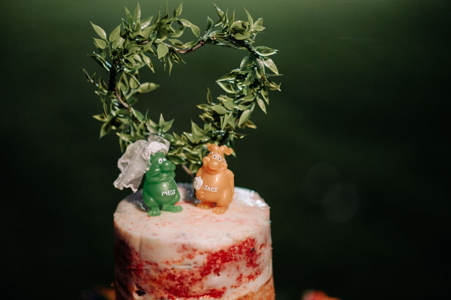 Wedding cake topped with cute animal figurines under leafy heart arch.