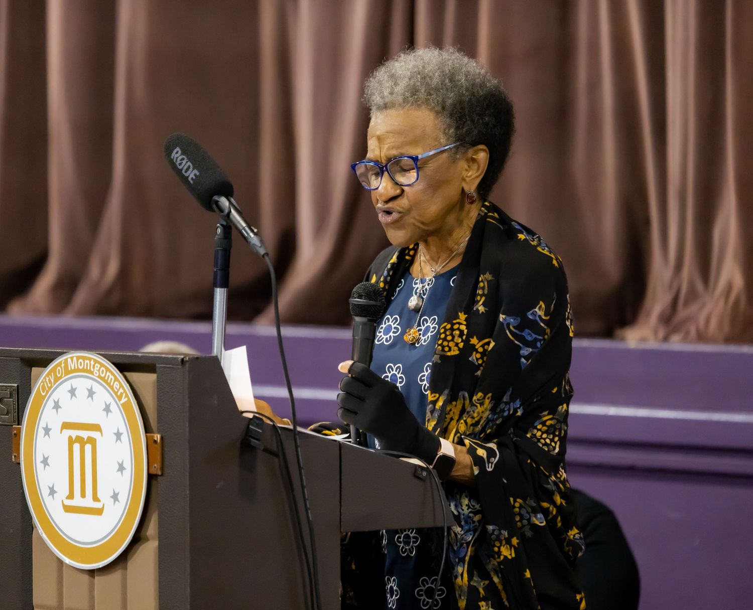 Speaker behind a podium delivers remarks at a podium with logo at formal event.