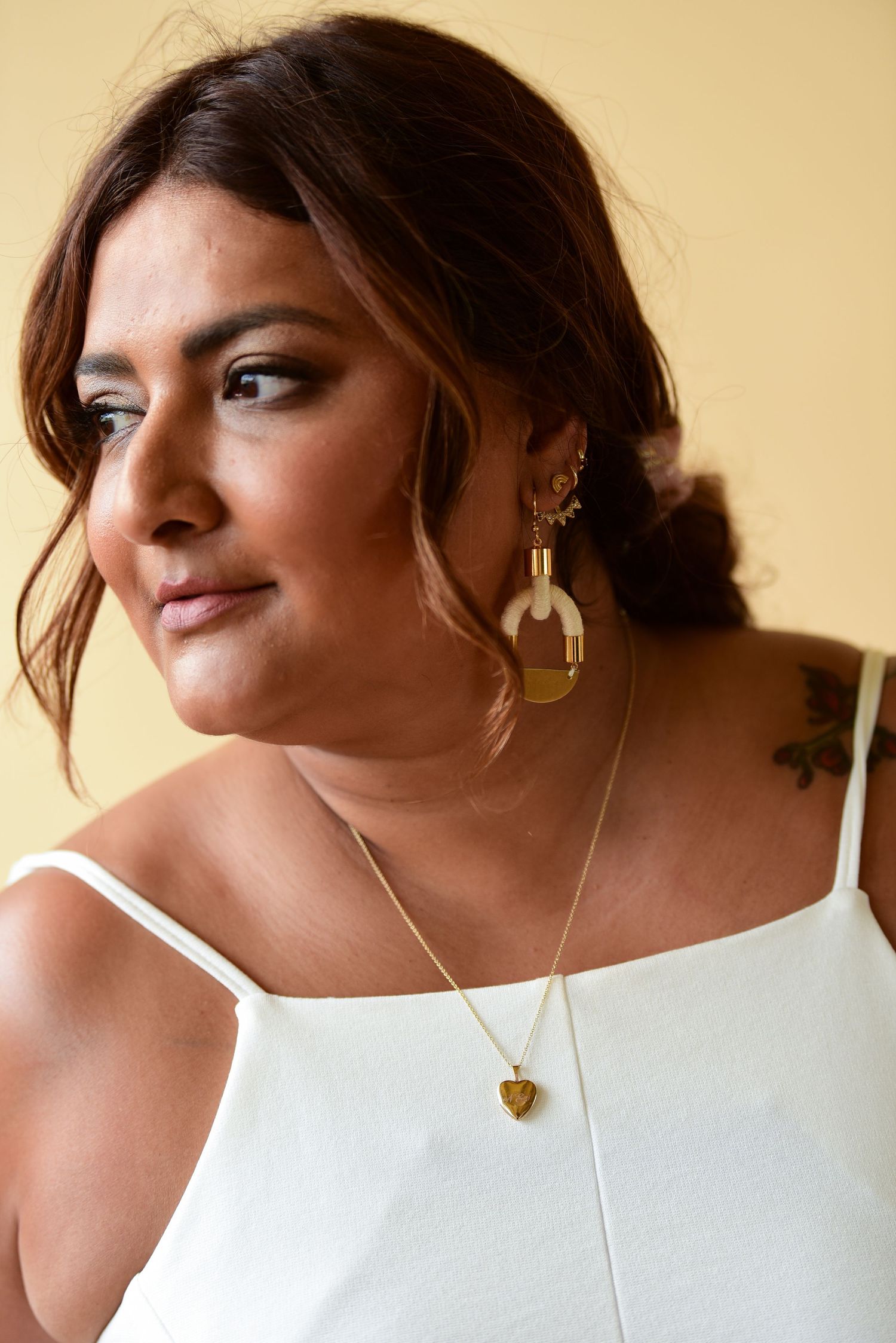 Elegant white camisole top accessorized with gold statement earrings and layered necklaces.