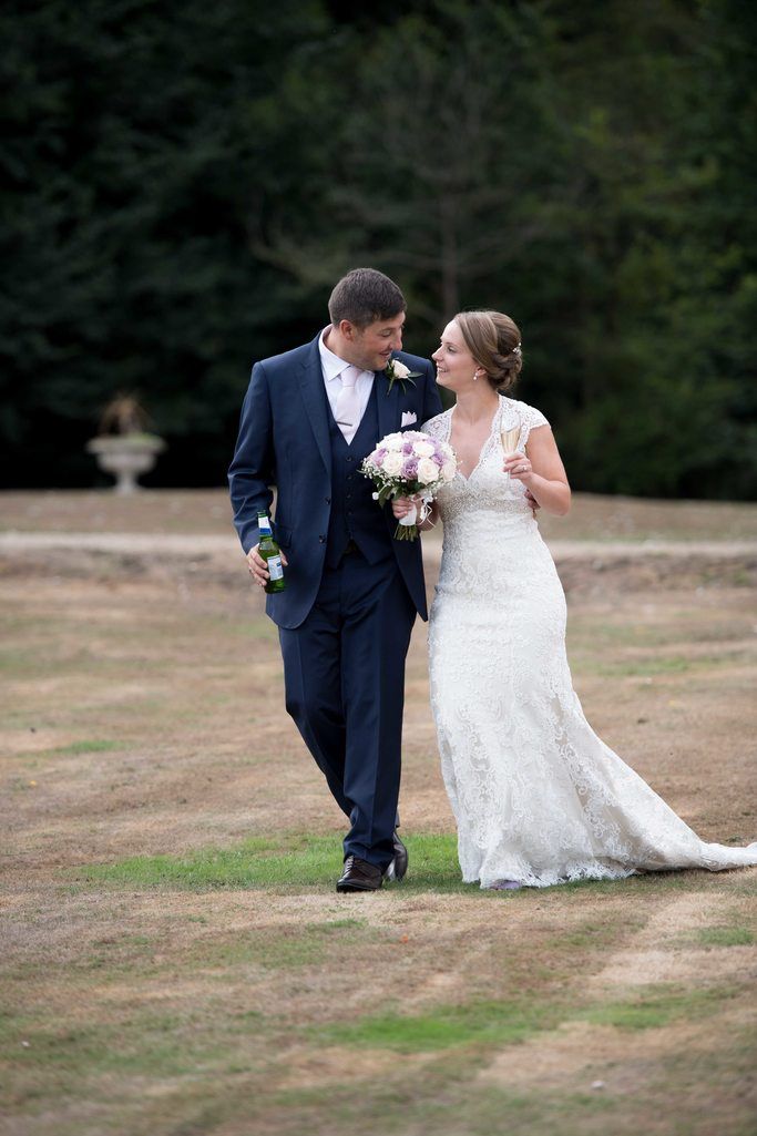 Couple walks together on estate grounds with bride holding pink bouquet.