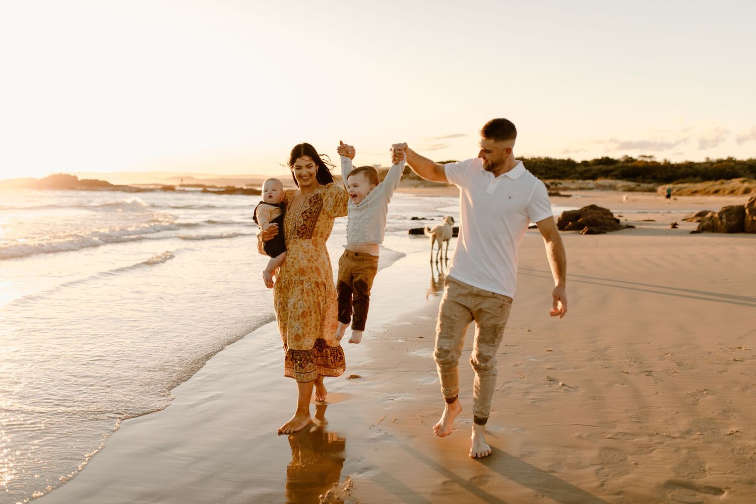 Family walking together on beach at sunset with waves washing ashore.