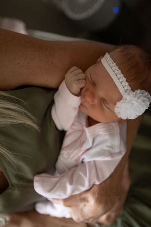 Sleeping newborn in pink outfit with white lace headband.