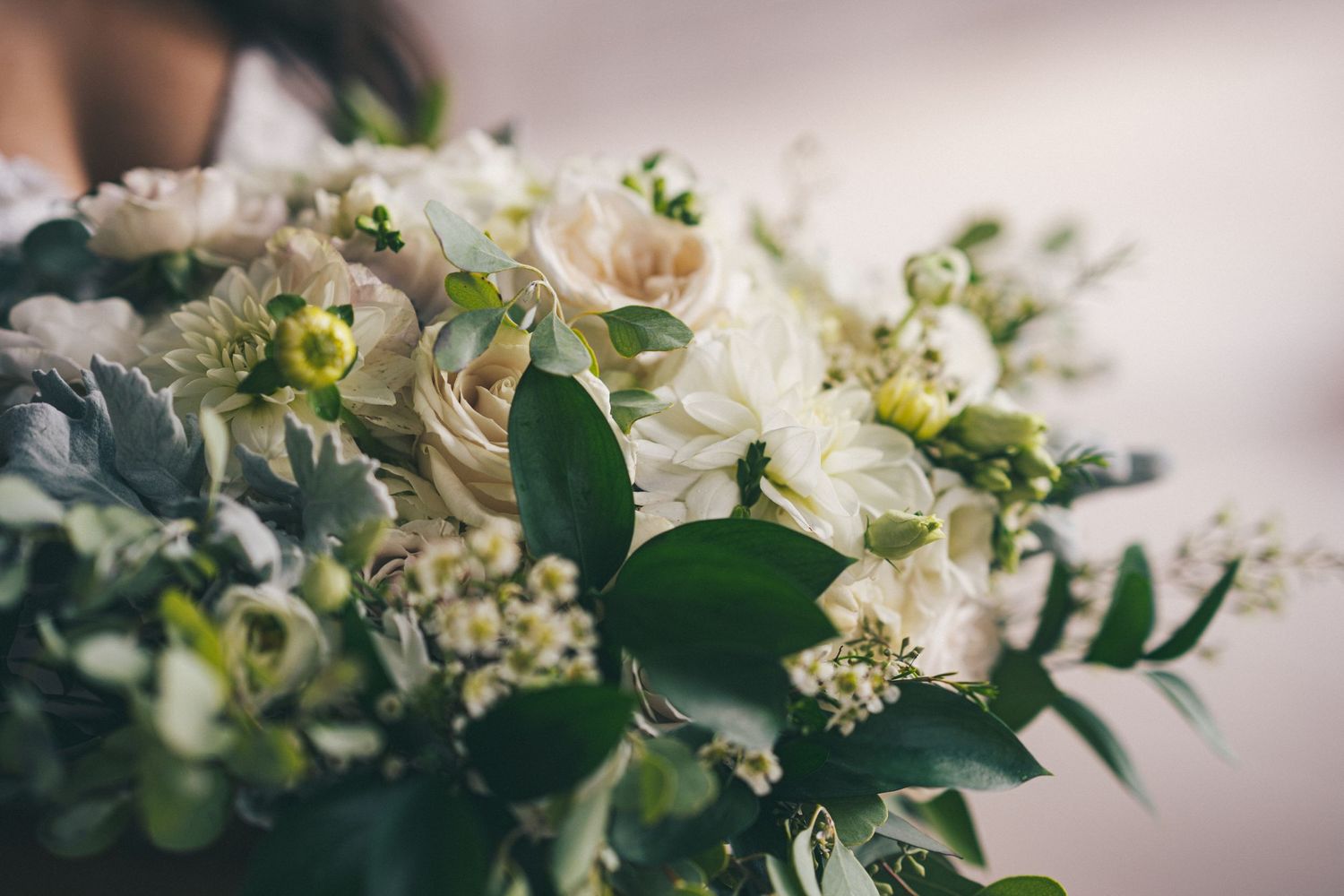 Elegant white floral arrangement with greenery in soft focus against blush background.