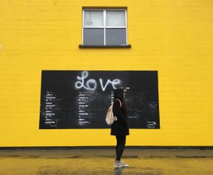 Person standing against bright yellow wall with 'Love' written in chalk.