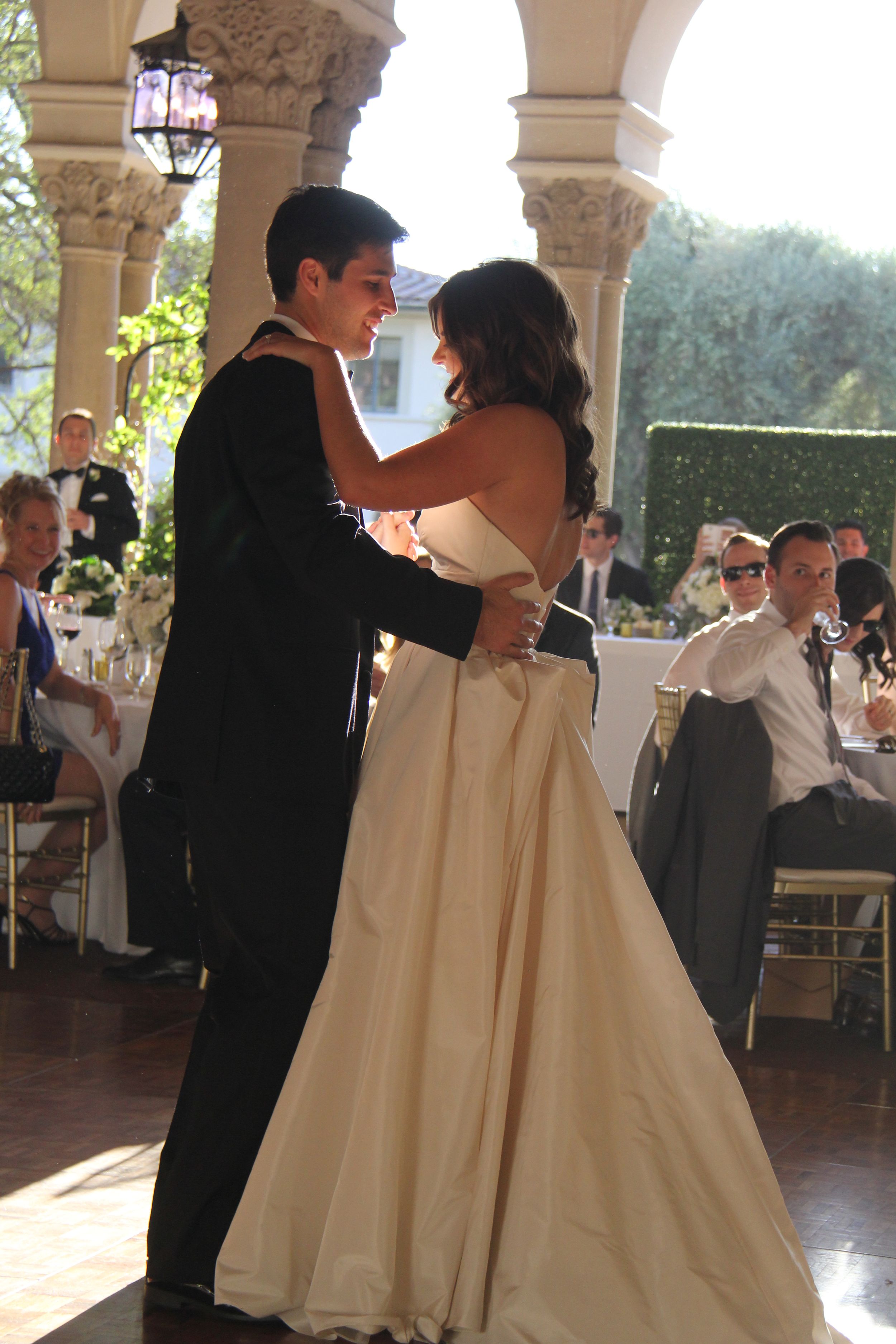 Newlyweds share their first dance under elegant stone archways at an outdoor reception.