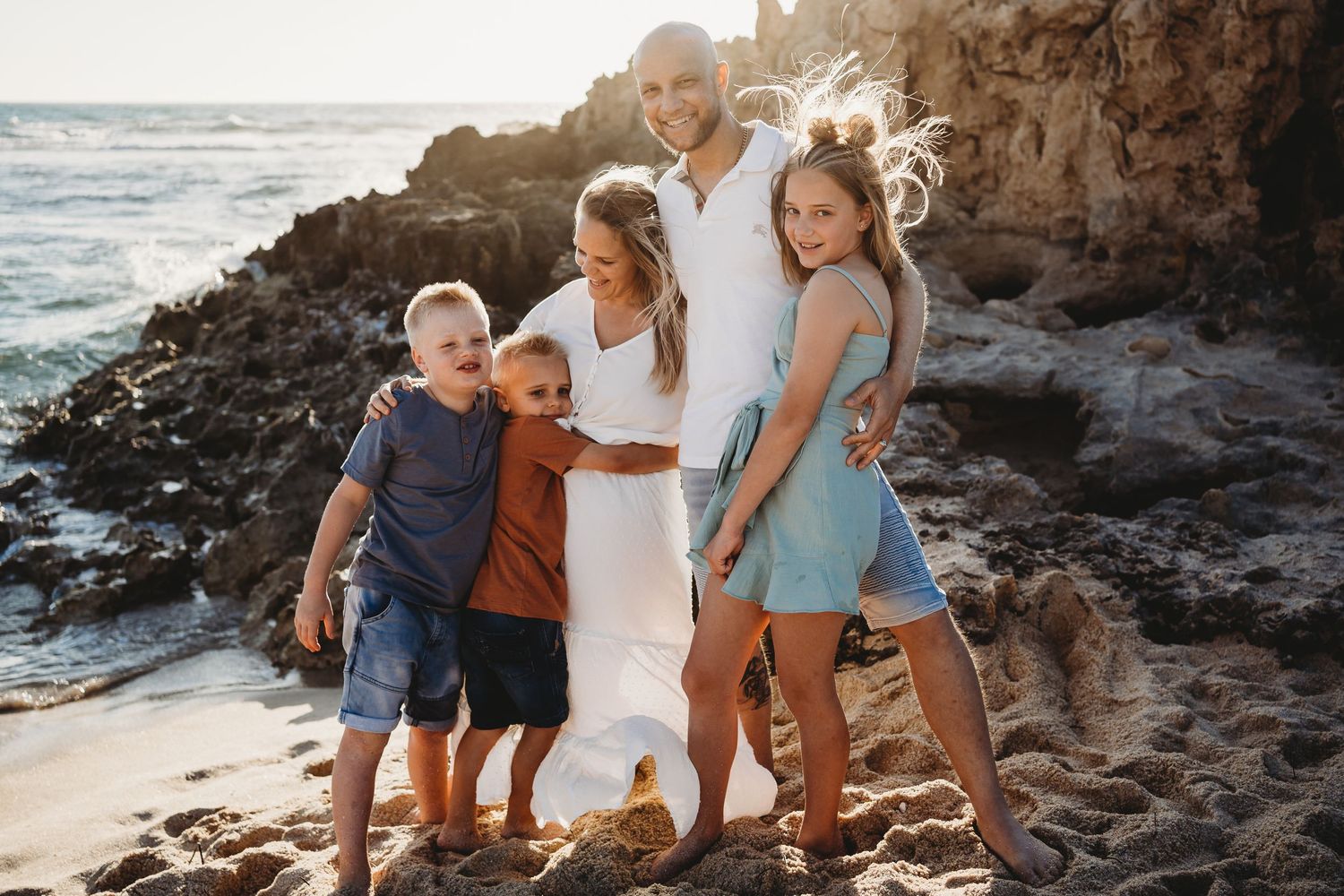 A family posing together on rocky coastal cliffs during golden hour.