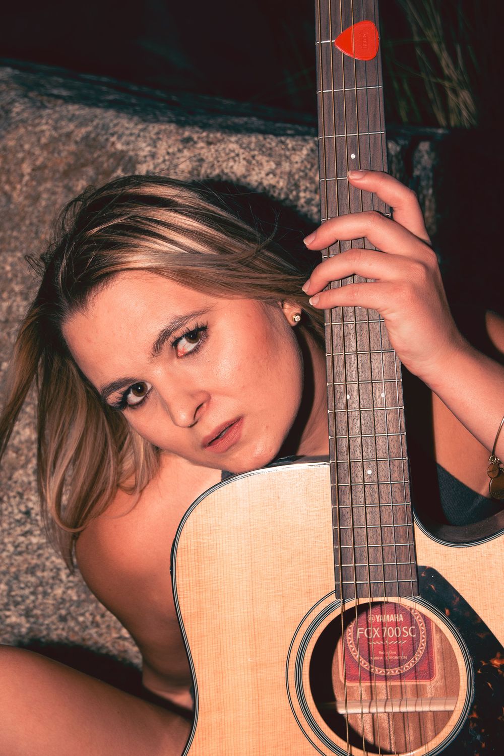 Woman with long hair poses with an acoustic guitar against a textured background.