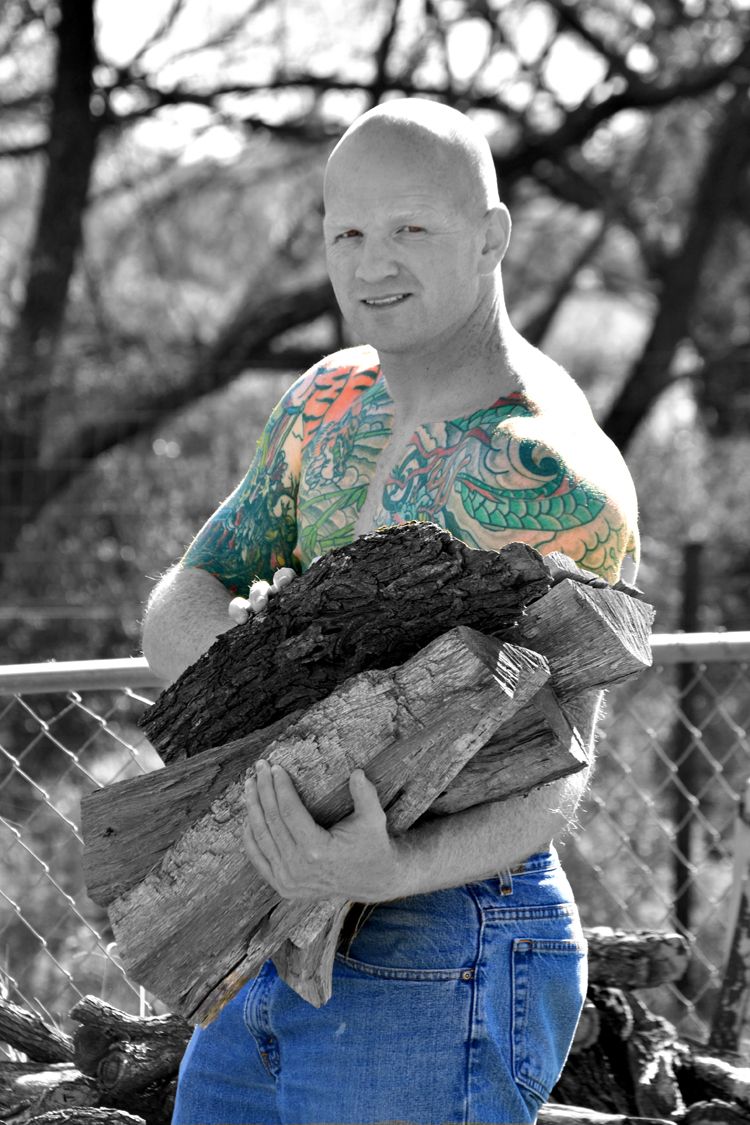 Man with tattoos holding a large bird outdoors in a black and white photo with selective color.