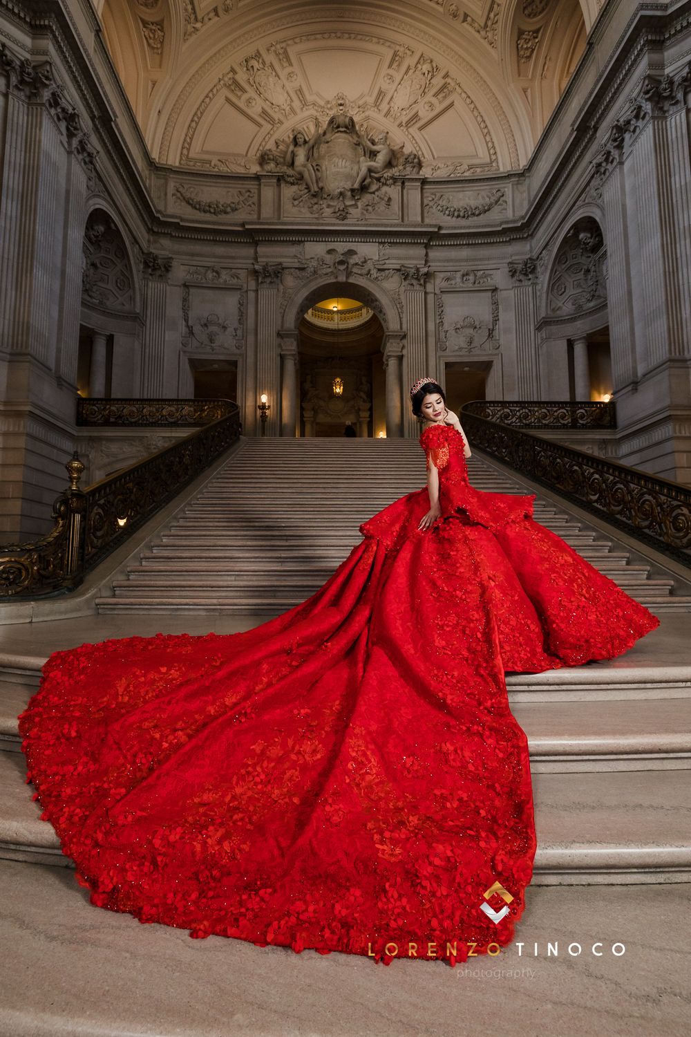 Dramatic red quinceañera dress with cathedral train displayed on ornate marble staircase.