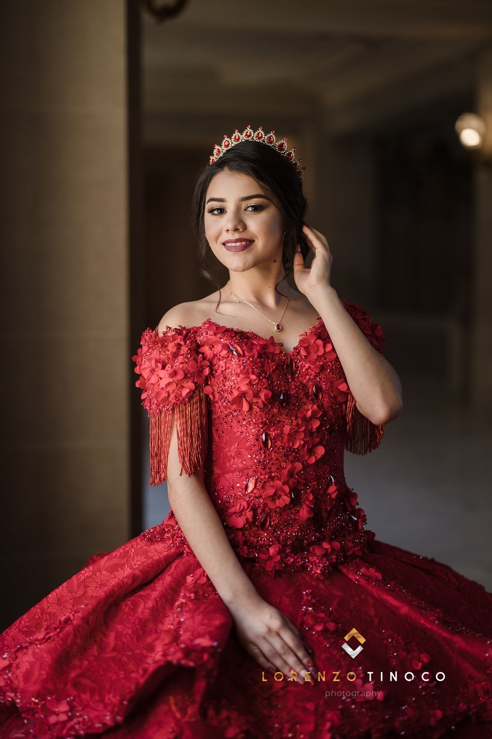A stunning red quinceanera gown with intricate beading and off-shoulder design photographed in dramatic lighting.