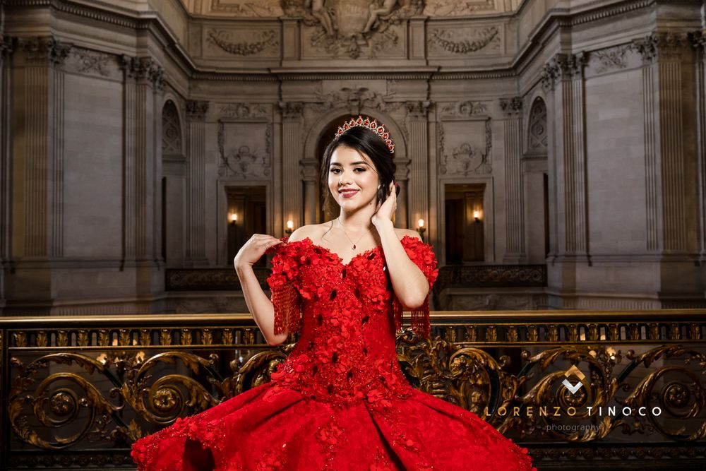Ornate red ball gown photographed in grand marble hall with decorative ceiling.