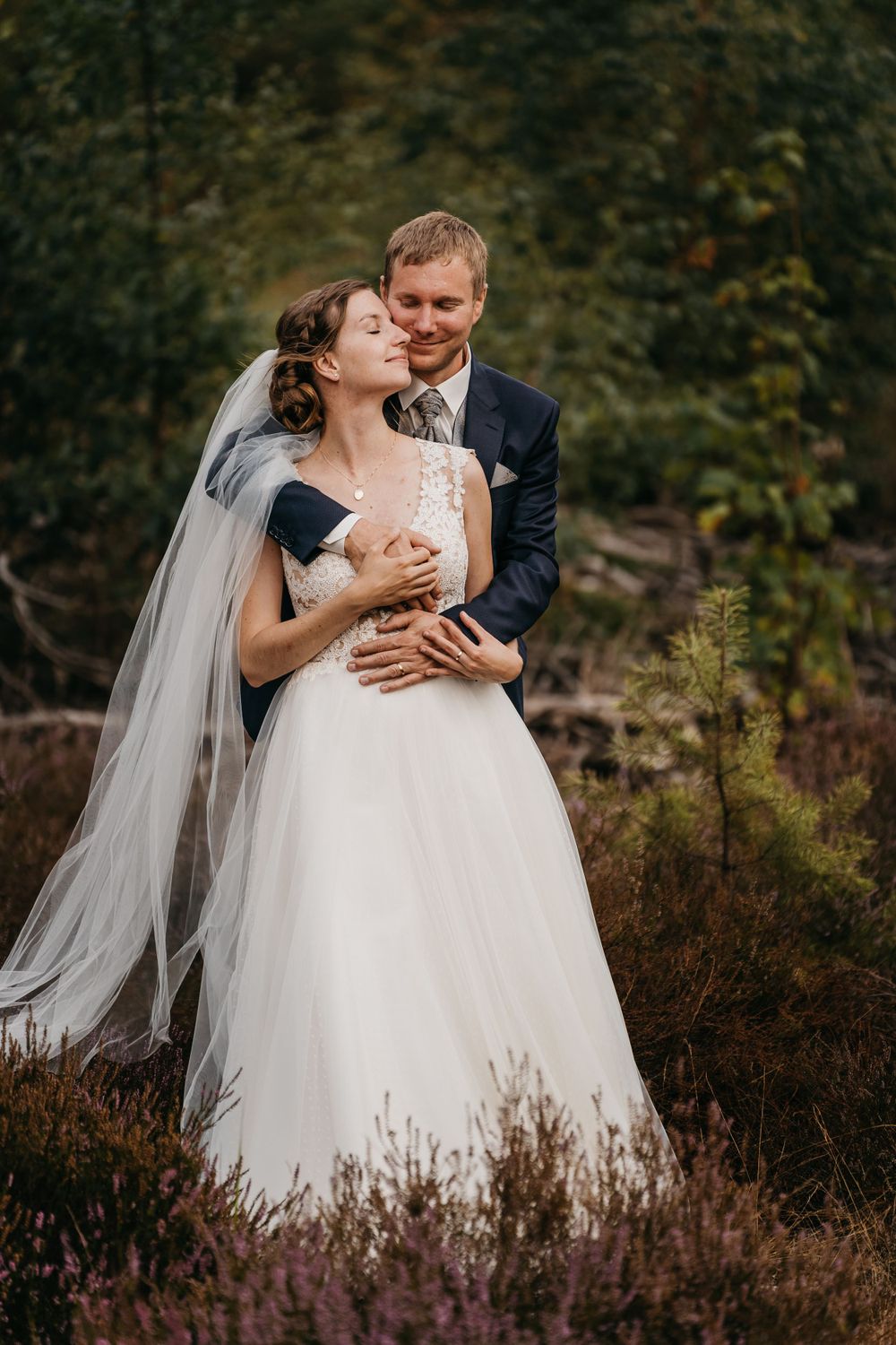Romantic wedding portrait of a couple embracing in a natural autumn setting with flowing veil.