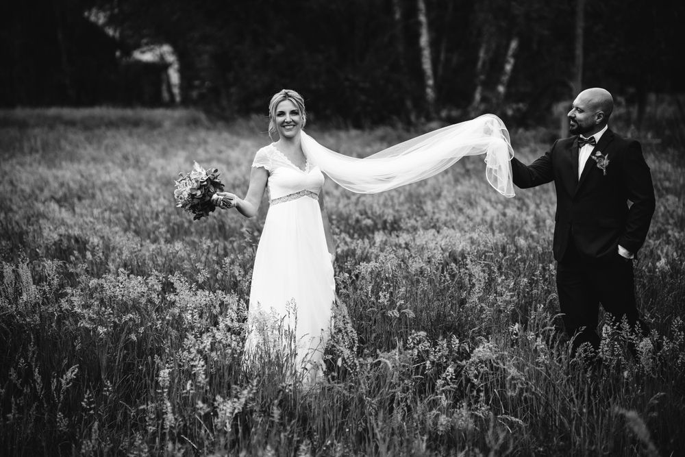 Black and white wedding photo of a couple in a meadow with bride's veil flowing in the wind.