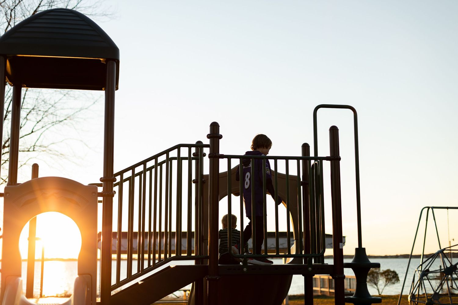 Silhouettes of children playing on playground structure at sunset.