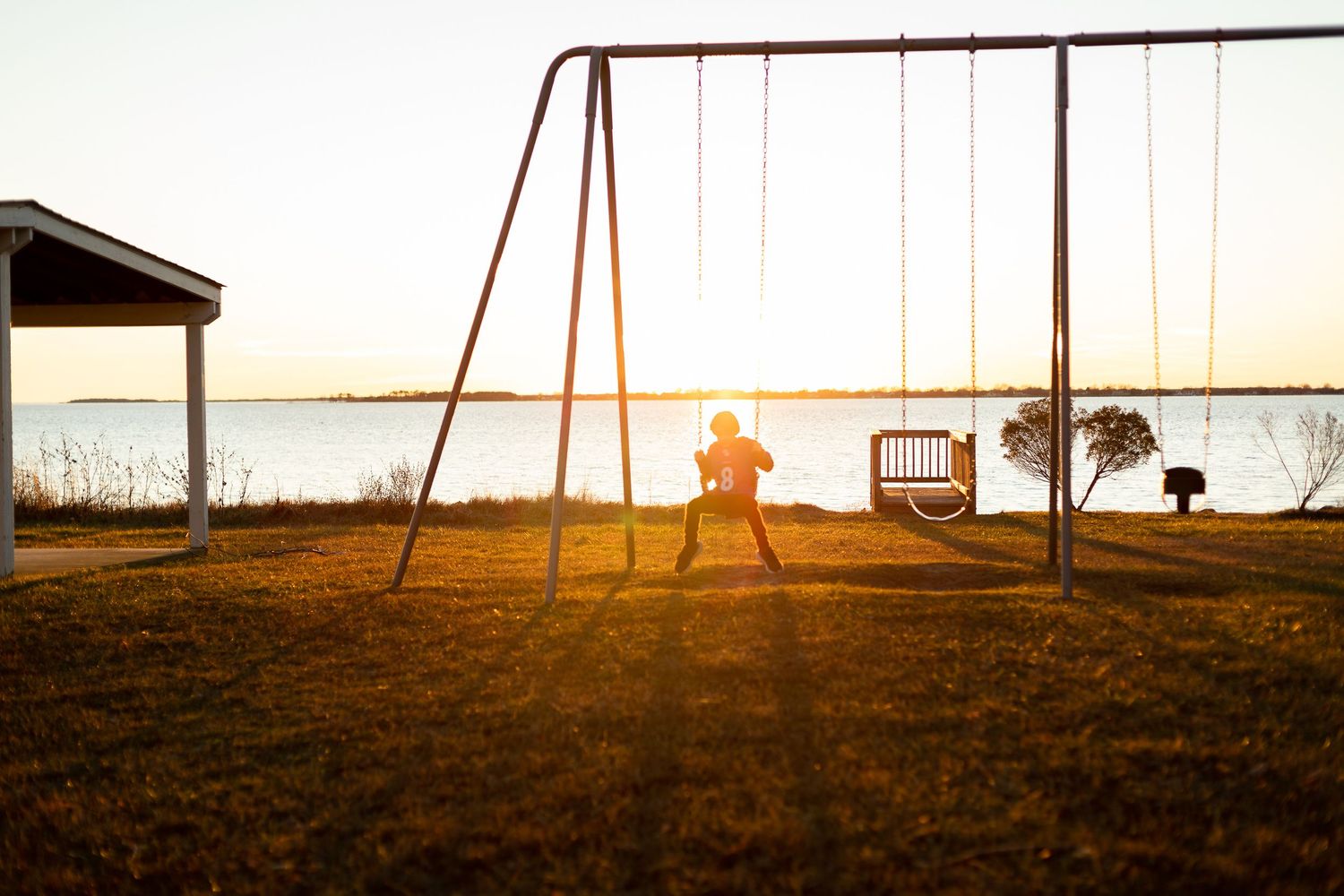 Empty swing set silhouetted against sunset sky near water.