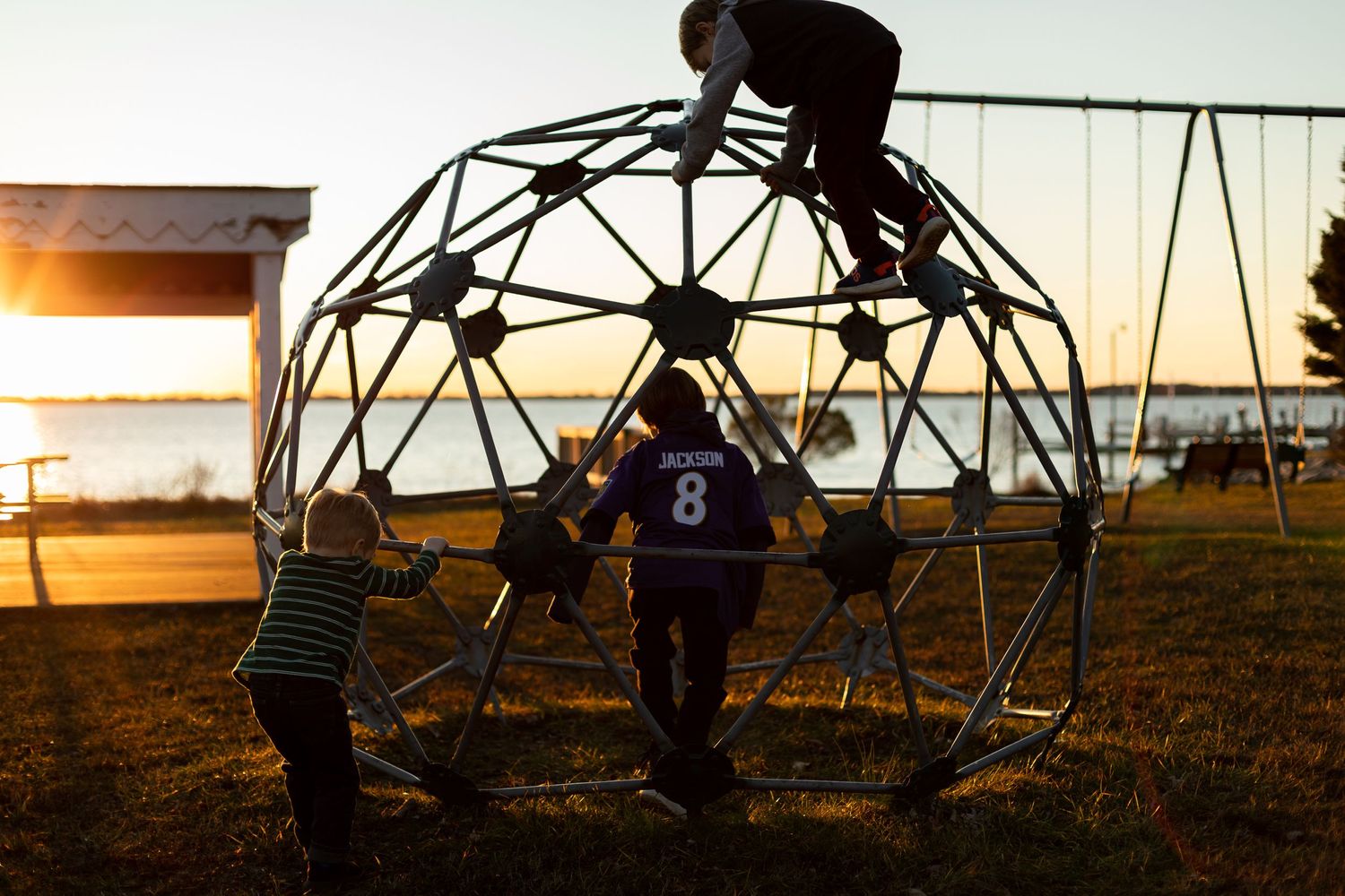 Children climbing on geodesic dome playground equipment at sunset.