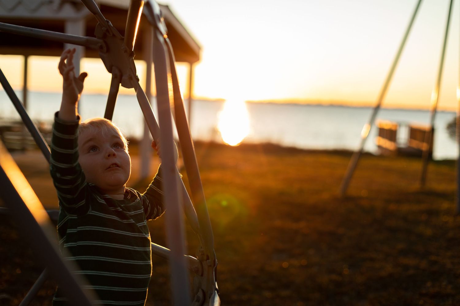 Child playing on playground equipment during golden hour sunset.