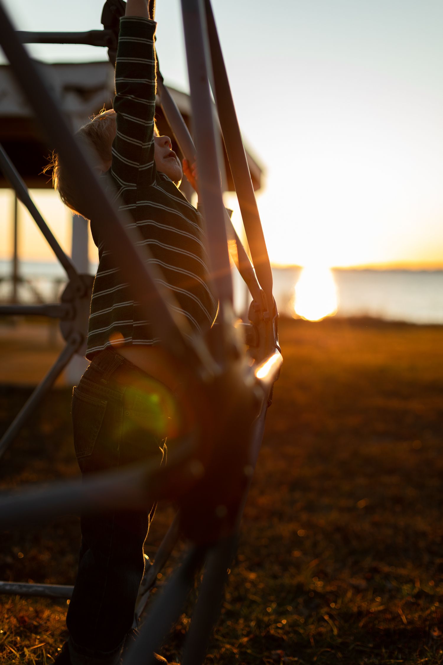Striped silhouette of playground equipment against sunset sky.