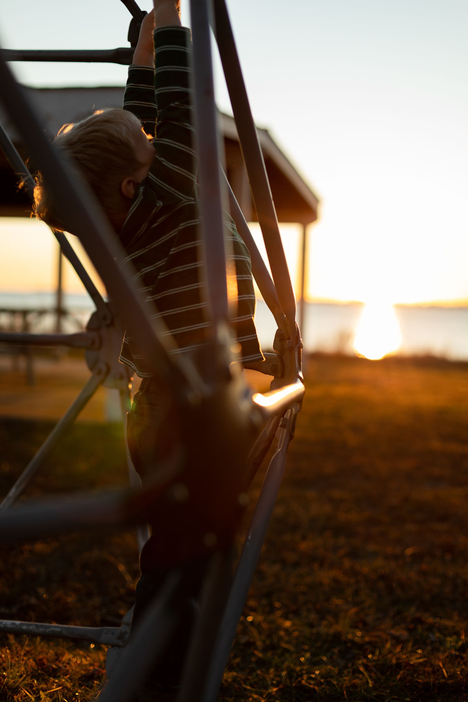 Child climbing on playground equipment with sunset in background.