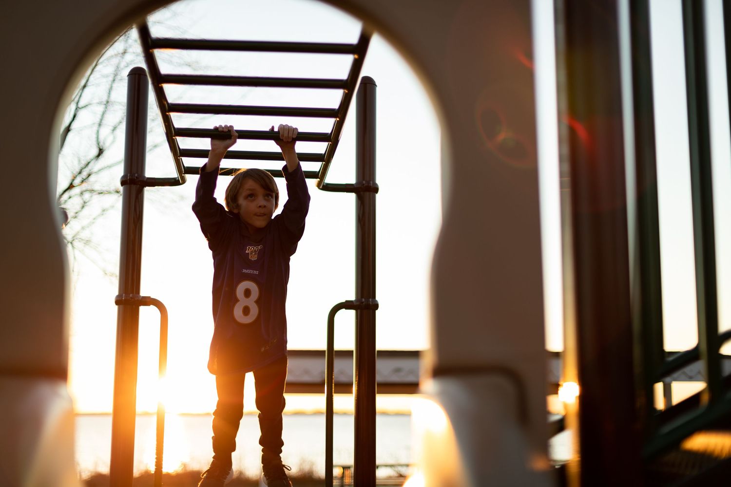 Silhouette of child hanging from playground bars at sunset.