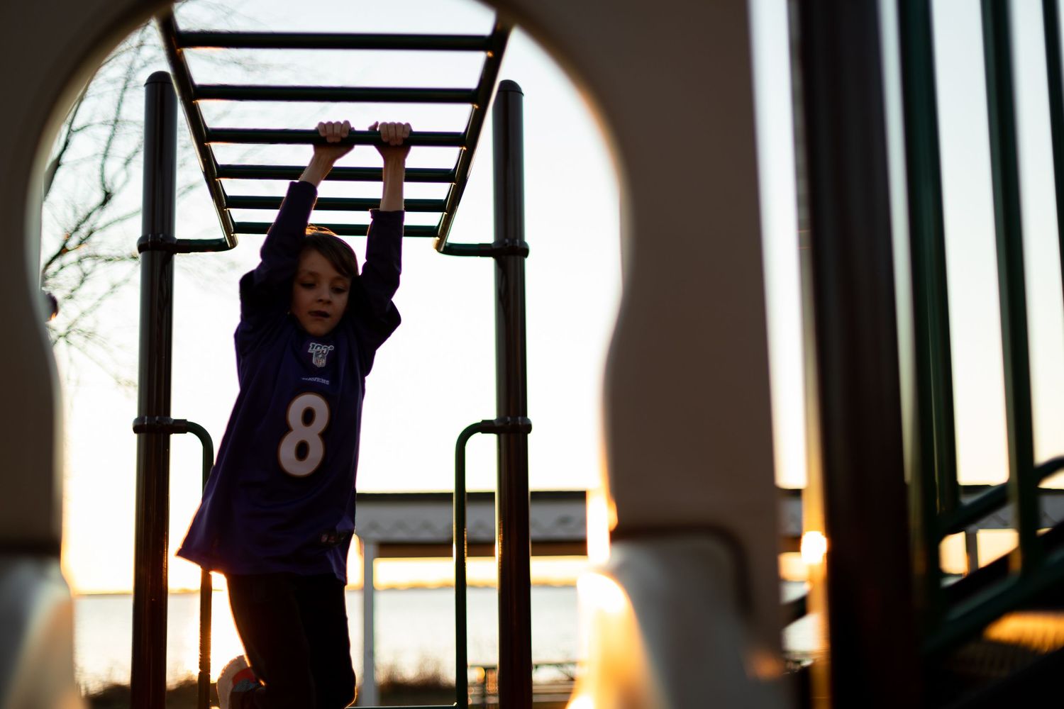 Child wearing jersey number 8 plays on playground equipment at sunset.