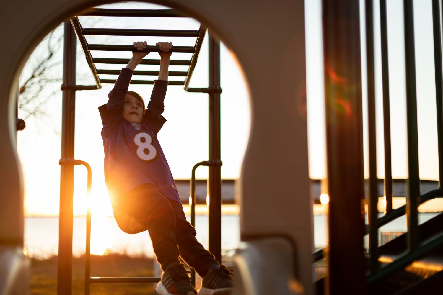 Silhouette of someone hanging from monkey bars during golden hour sunset.