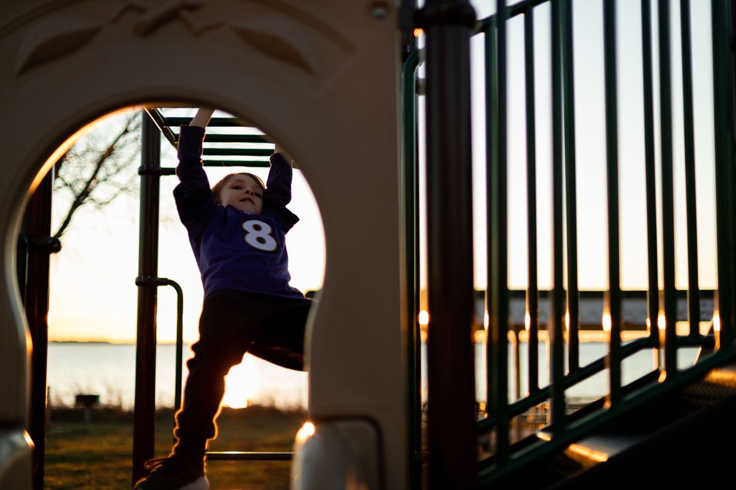 Athletic figure climbing on playground equipment framed by archway at sunset.