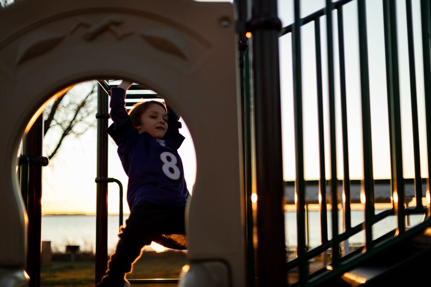 Silhouetted figure playing on playground equipment against evening sky.