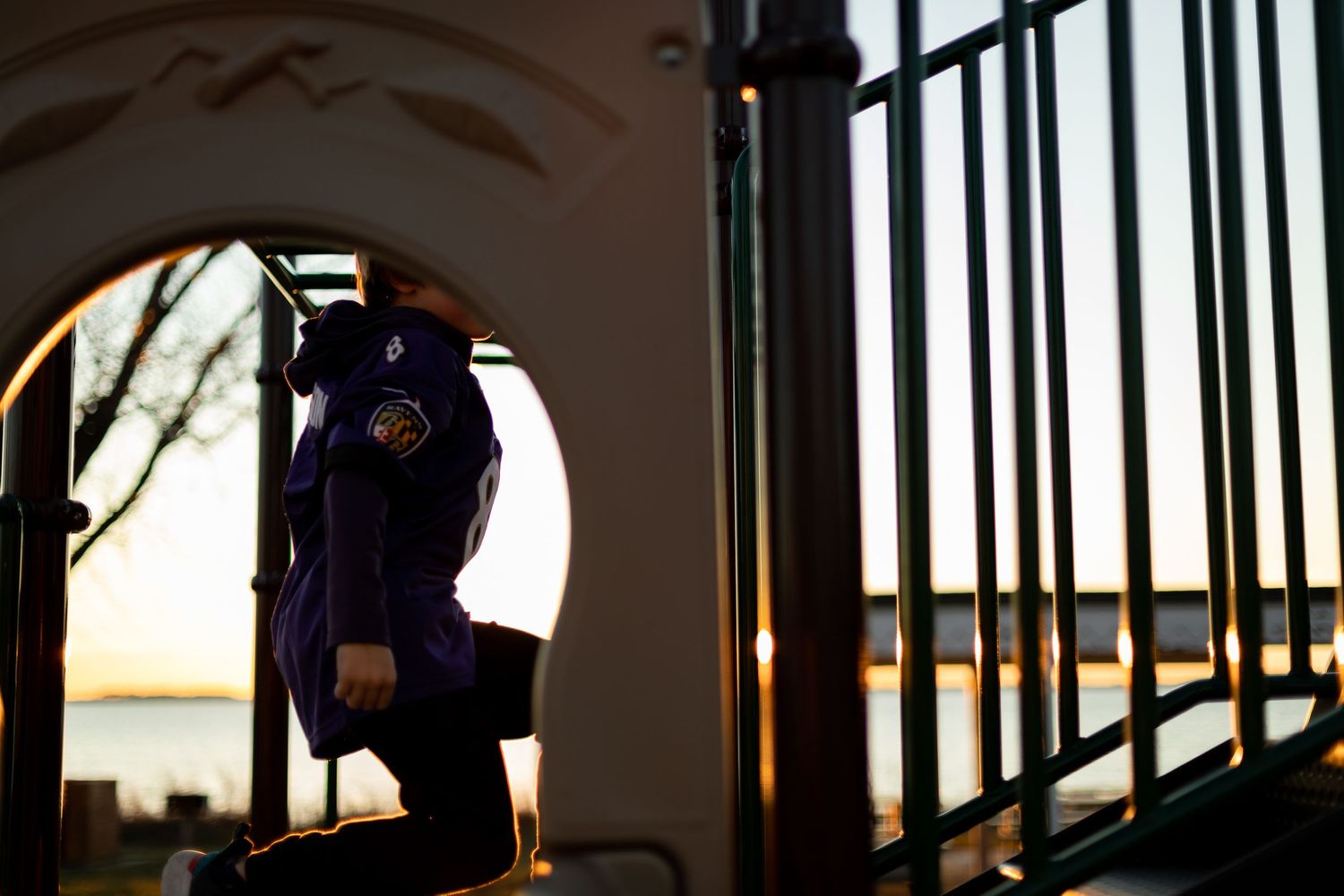 Dark silhouette climbing playground equipment through arched frame at dusk.