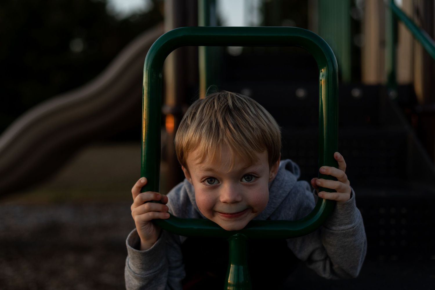 Child playing on green playground equipment at dusk.
