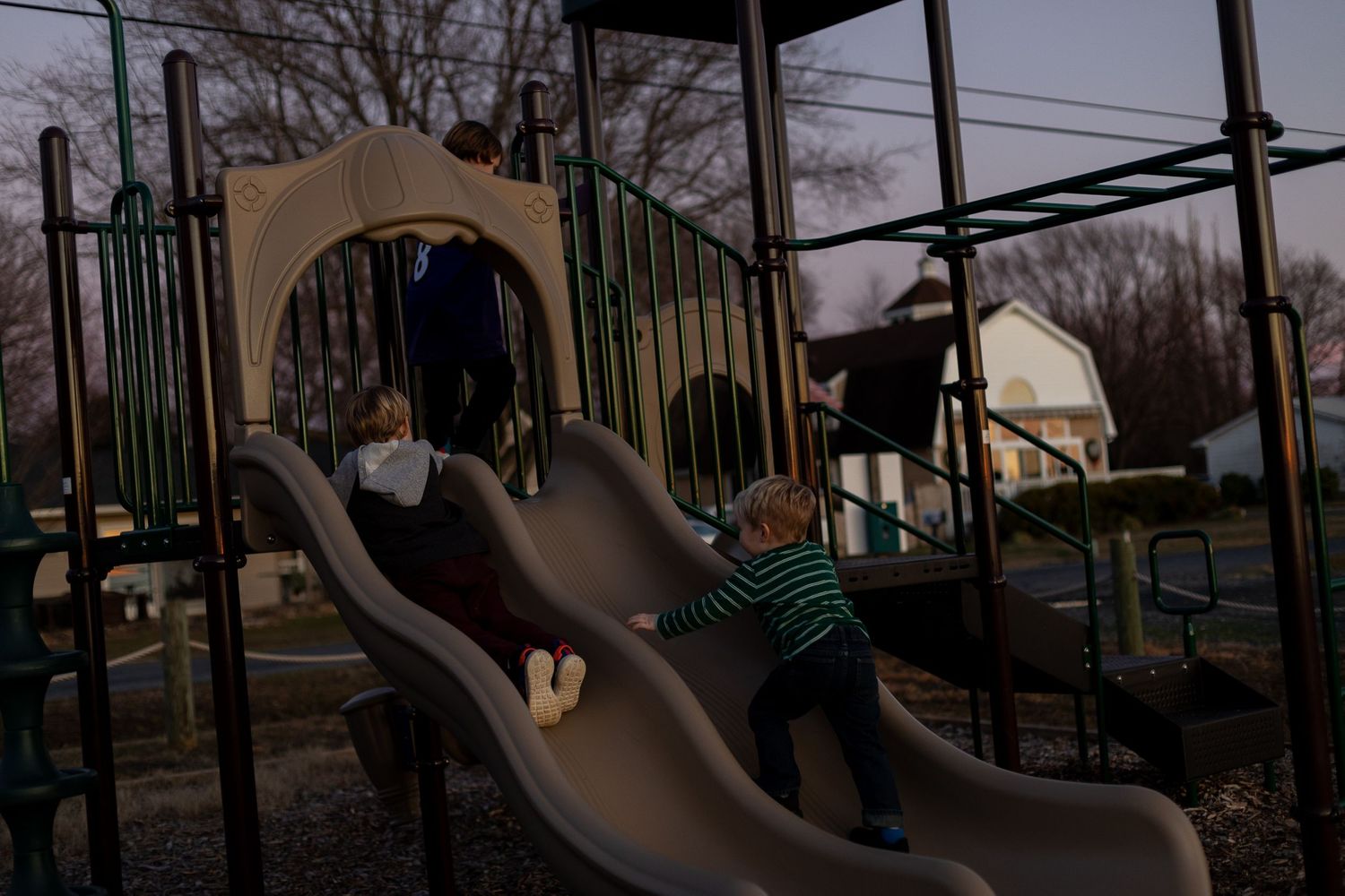 Children playing on playground slides at twilight.