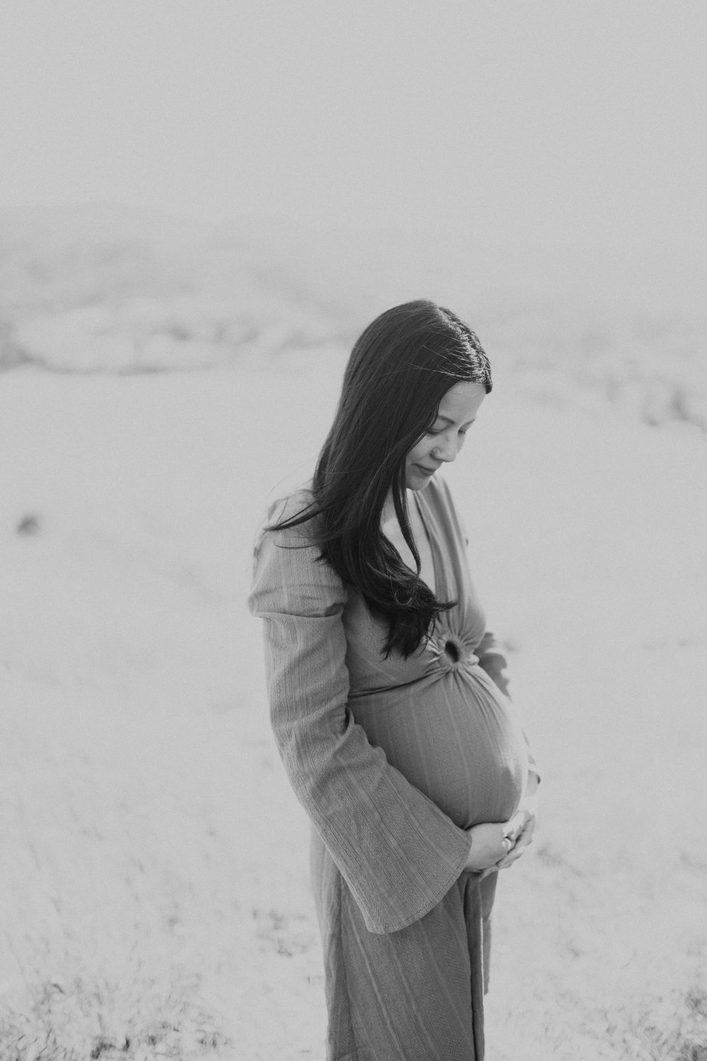 Black and white portrait of expecting mother holding her belly against minimalist background.