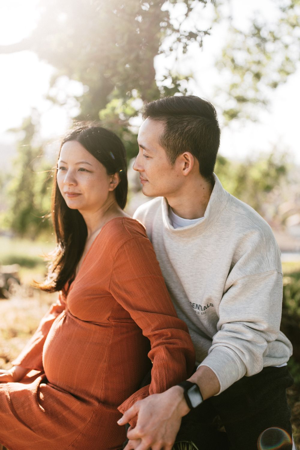 An intimate maternity portrait of a couple sitting together in warm sunlight.