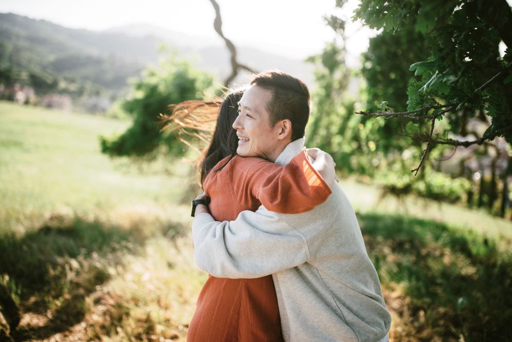 Sweet embrace captured in warm sunlight with twisted tree branch and rolling hills behind.