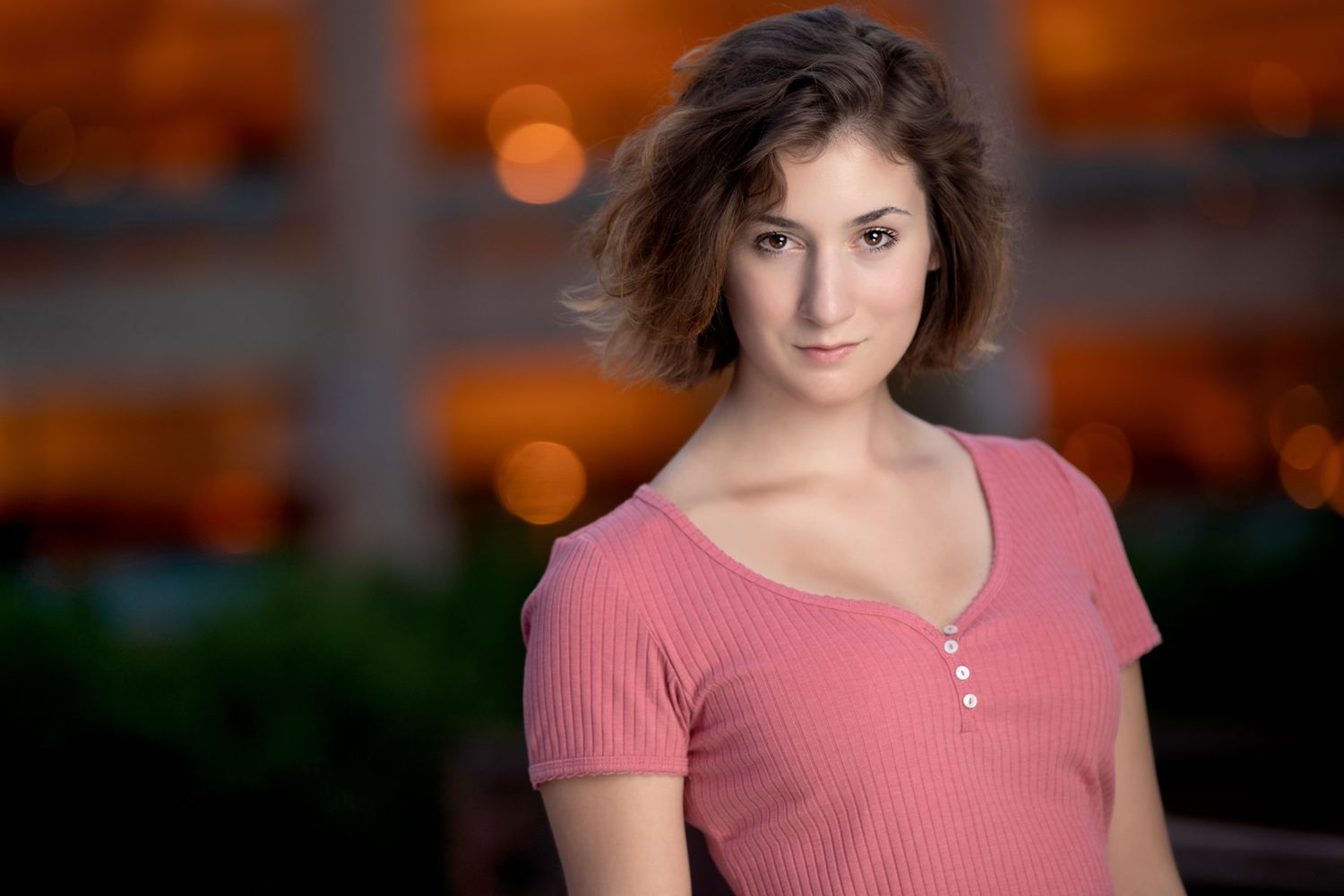 Portrait against blurred orange bokeh background wearing a pink ribbed shirt.