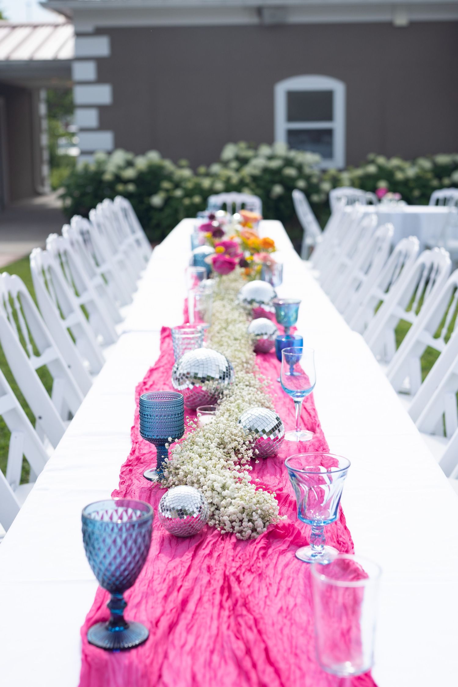 Wedding reception setup with white chairs and pink table runner decorated with baby's breath centerpieces.