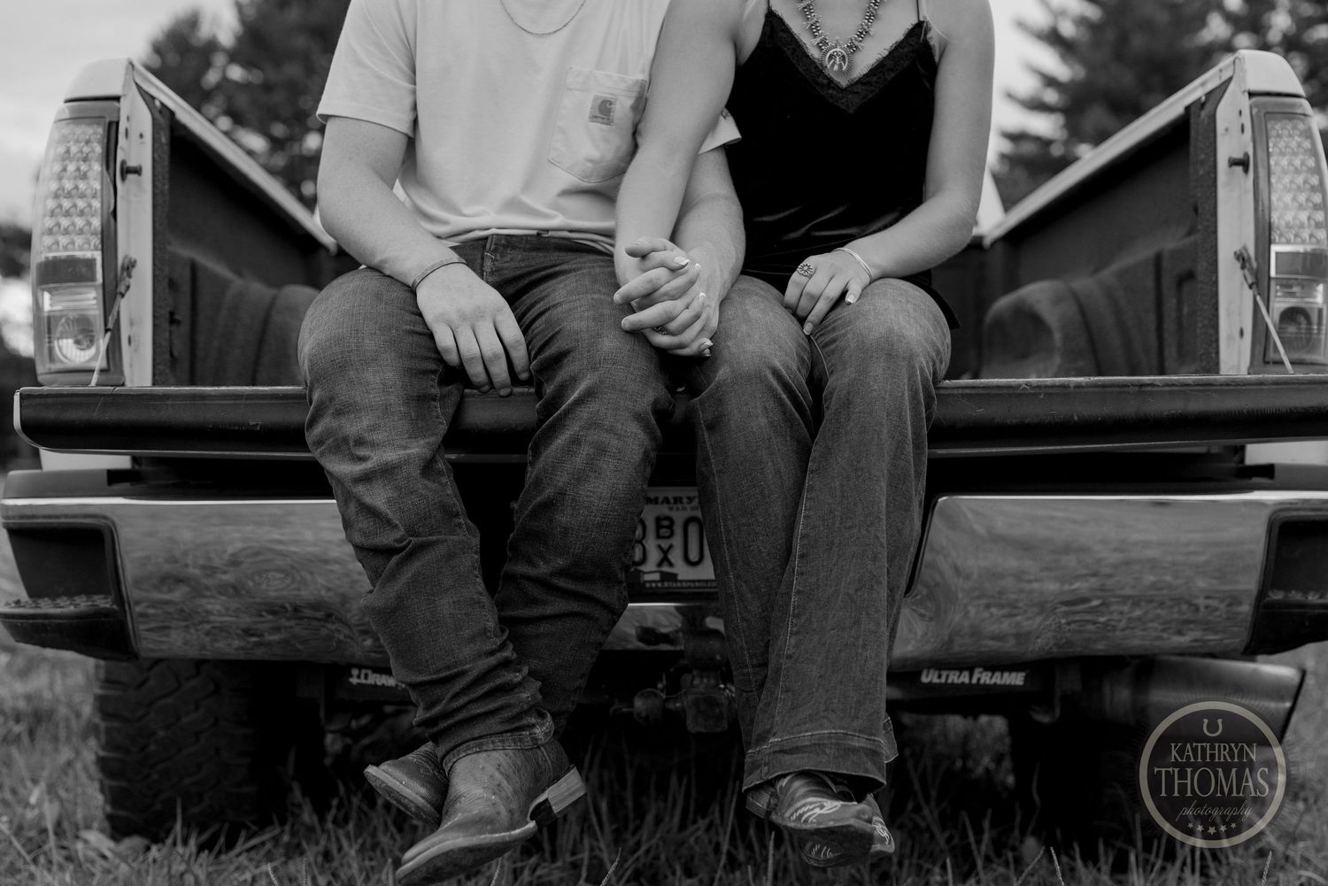 A black and white portrait of a couple sitting on the tailgate of a pickup truck.