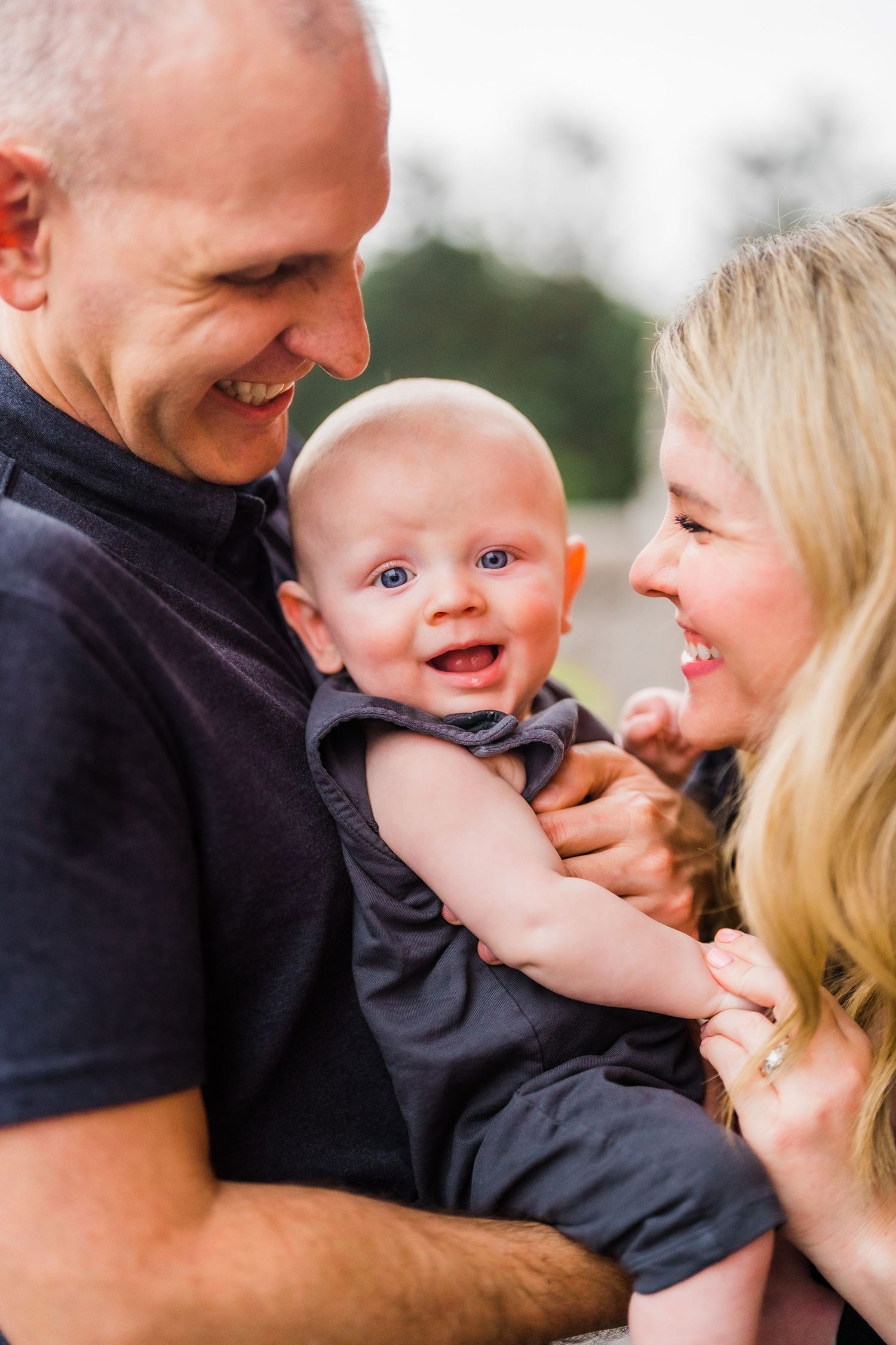 Happy family shares loving moment with smiling baby in casual outdoor setting.