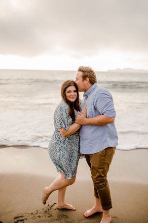 Couple sharing affectionate moment on sandy beach with overcast sky.