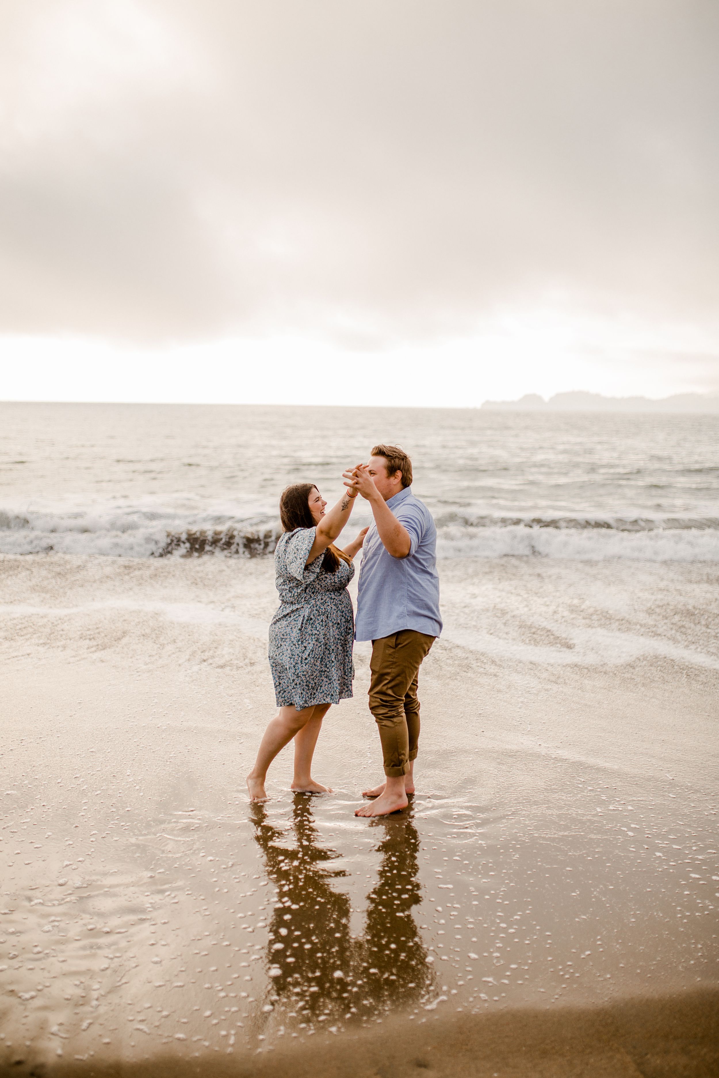 Couple playing in the ocean waves during golden hour on cloudy beach.